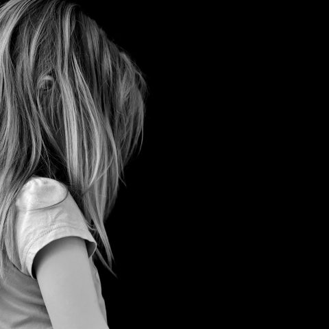 Perfil de una niña tapado por el cabello largo rubio. Fondo negro