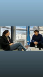 Bárbara y Daniel Arroyo sentados uno frente al otro en un sillón del despacho de Arroyo. Ventanales de fondo y una gran bandera argentina